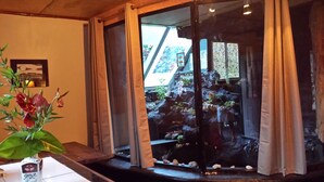 A room with a glass door leading to a rock garden, a vase with dried flowers, and a framed picture on the wall. - Aloha Crater Lodge (Volcano)
