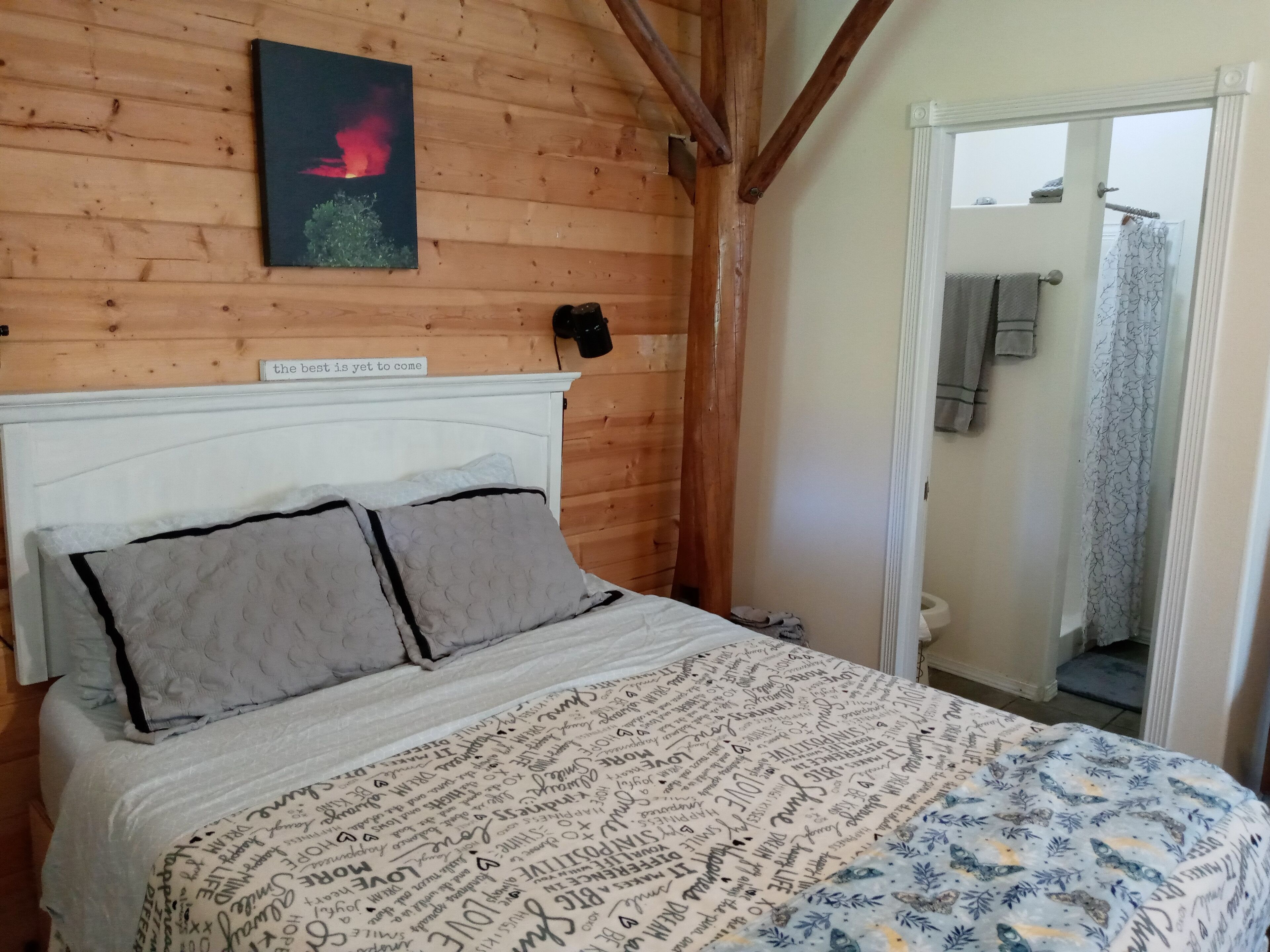 A wooden-paneled bedroom with a bed, a framed quote on the wall, and a bathroom visible through an open door.