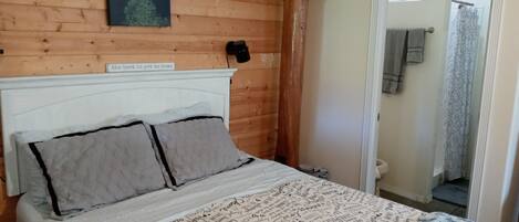 A wooden-paneled bedroom with a bed, a framed quote on the wall, and a bathroom visible through an open door.