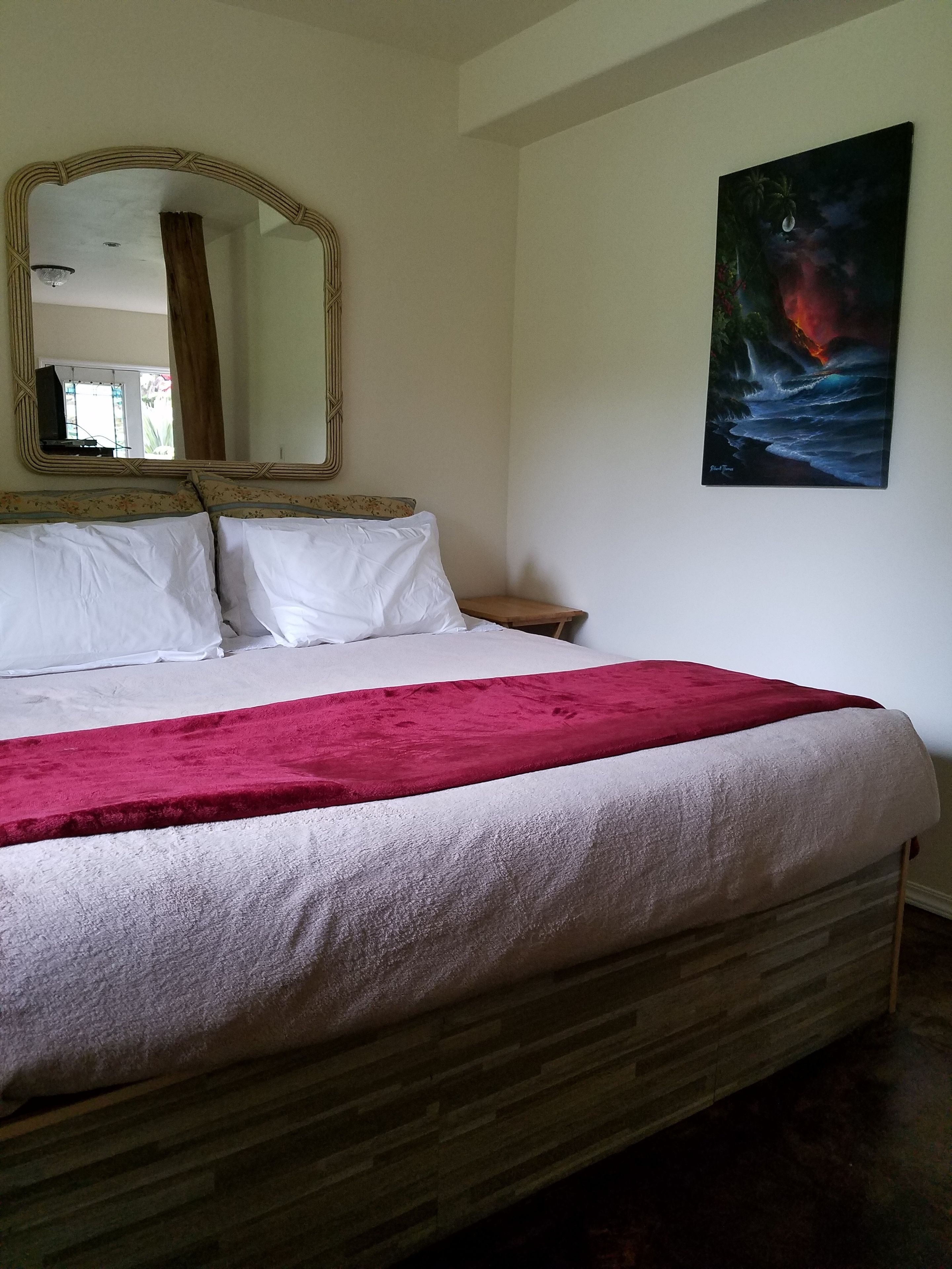 Un dormitorio con cama, espejo, mesita de noche y un cuadro en la pared.