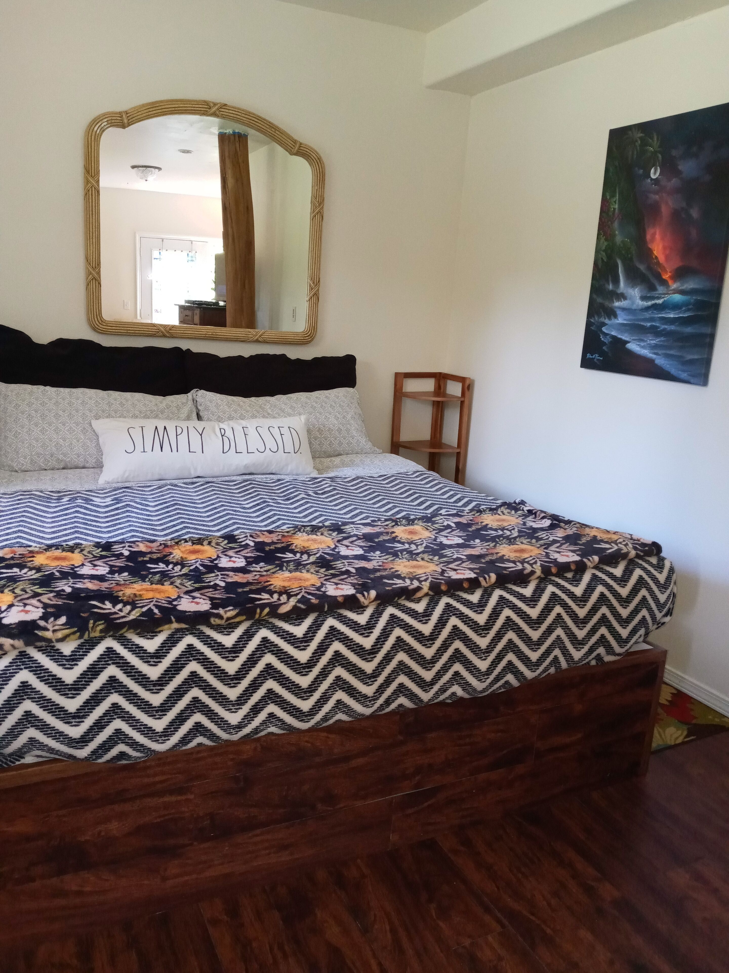 A bedroom with a bed, a mirror, a chair, and a painting on the wall.