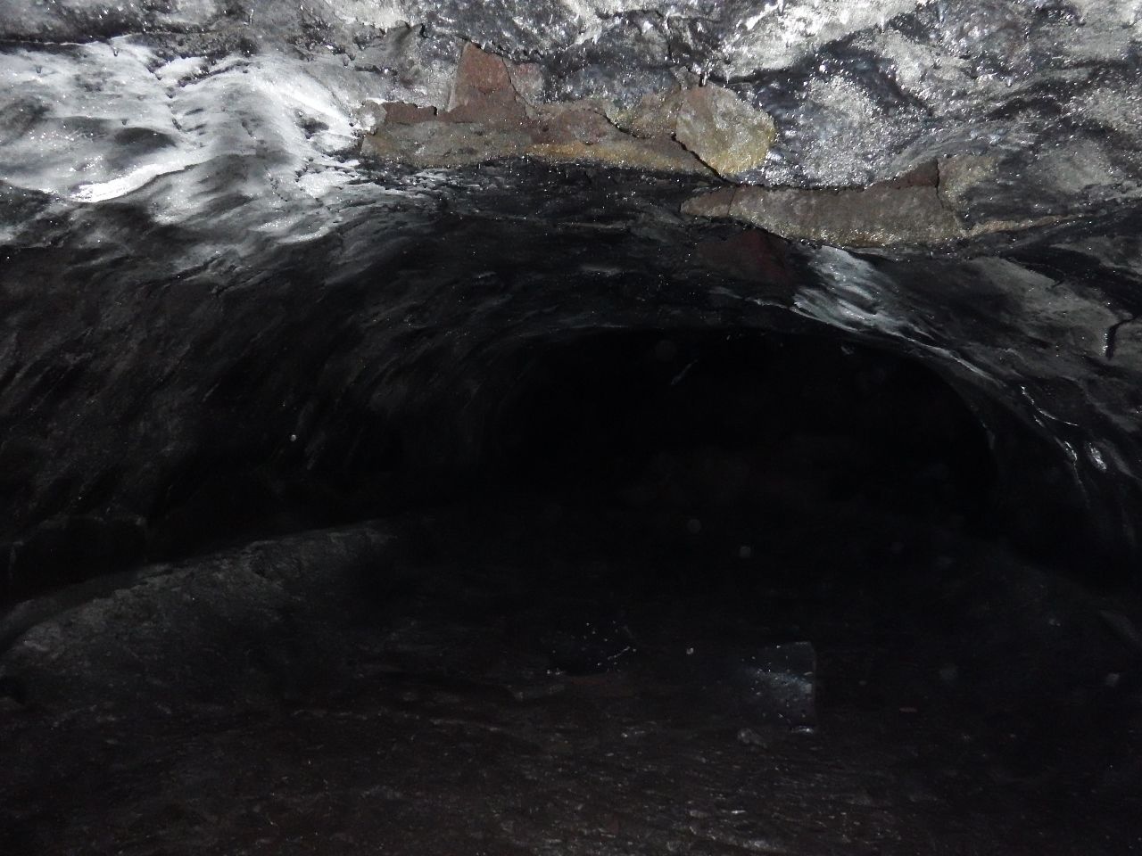 A dark, narrow tunnel with rough, uneven walls and a wet floor.