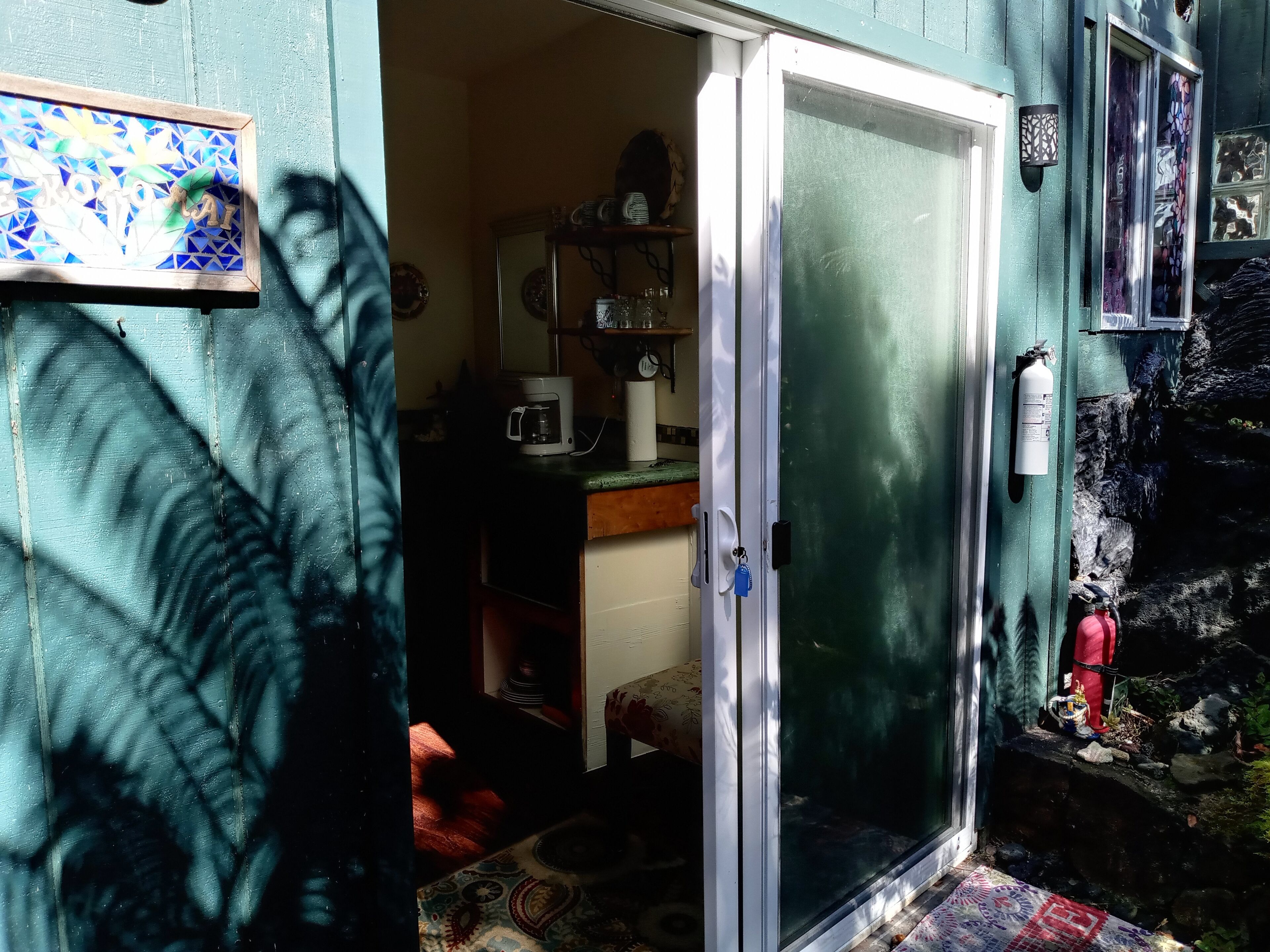 A room with a sliding glass door, a coffee maker, and a shelf with various items.