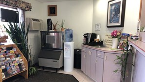 A small, well-lit room with a kitchenette, a water dispenser, a coffee machine, and a variety of books on a shelf. - Wilbraham Inn (Wilbraham)