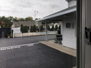 A view through a window with a metal grid, displaying a parking lot with a few cars and a building in the background.