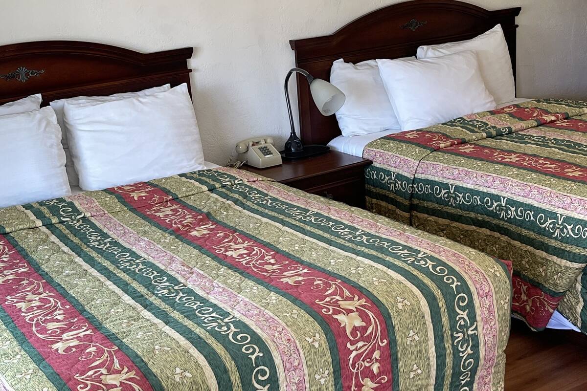 Duas camas de casal com cabeceiras de madeira, almofadas brancas e um cobreleito estampado.