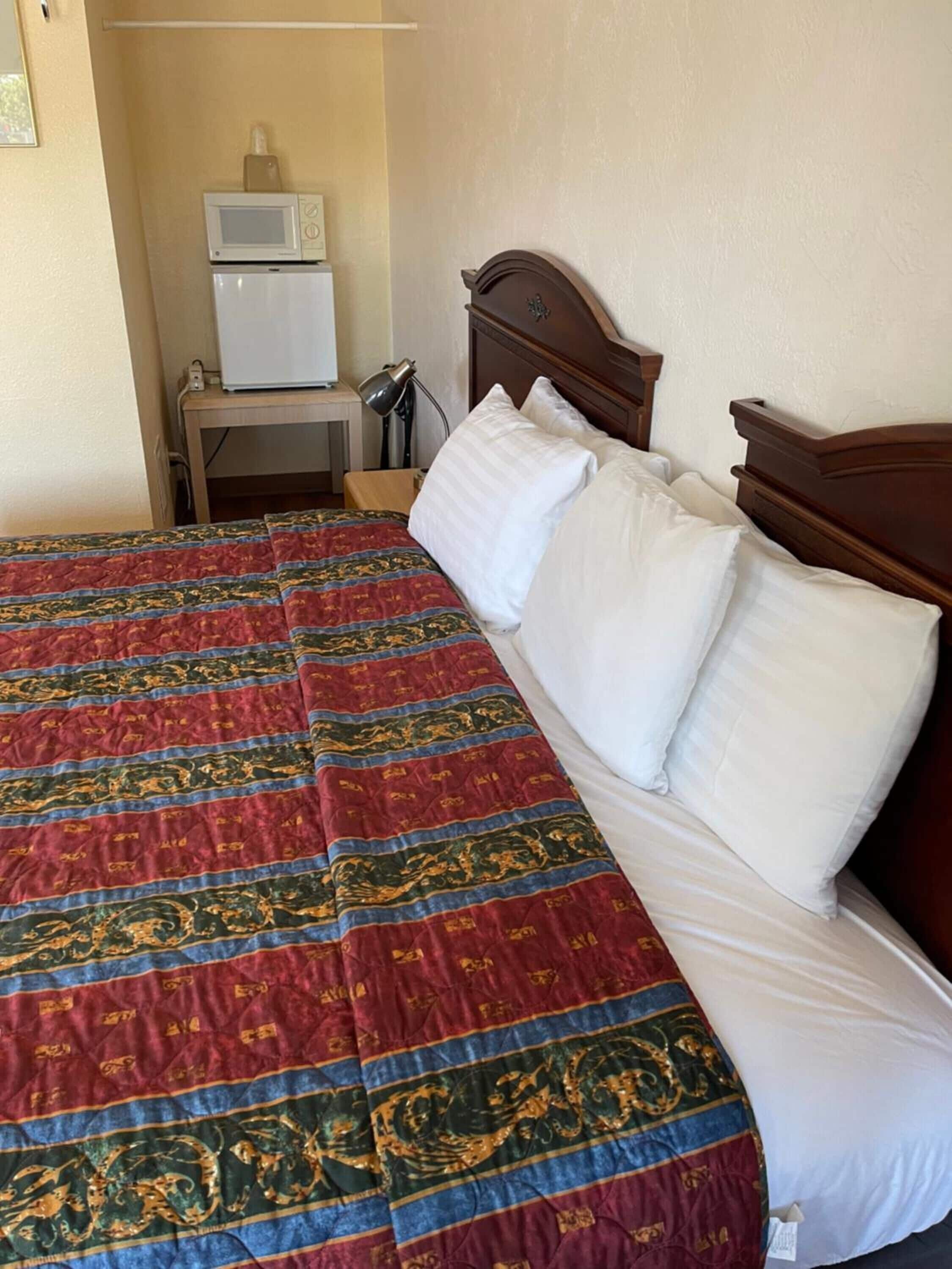 Una habitación de hotel con una cama, una mesita de noche, una lámpara, un microondas y un refrigerador.