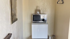 A compact hotel room with a bed, bedside table, a small desk with a lamp, a microwave, and a telephone. - Villa West Motel (Florence)