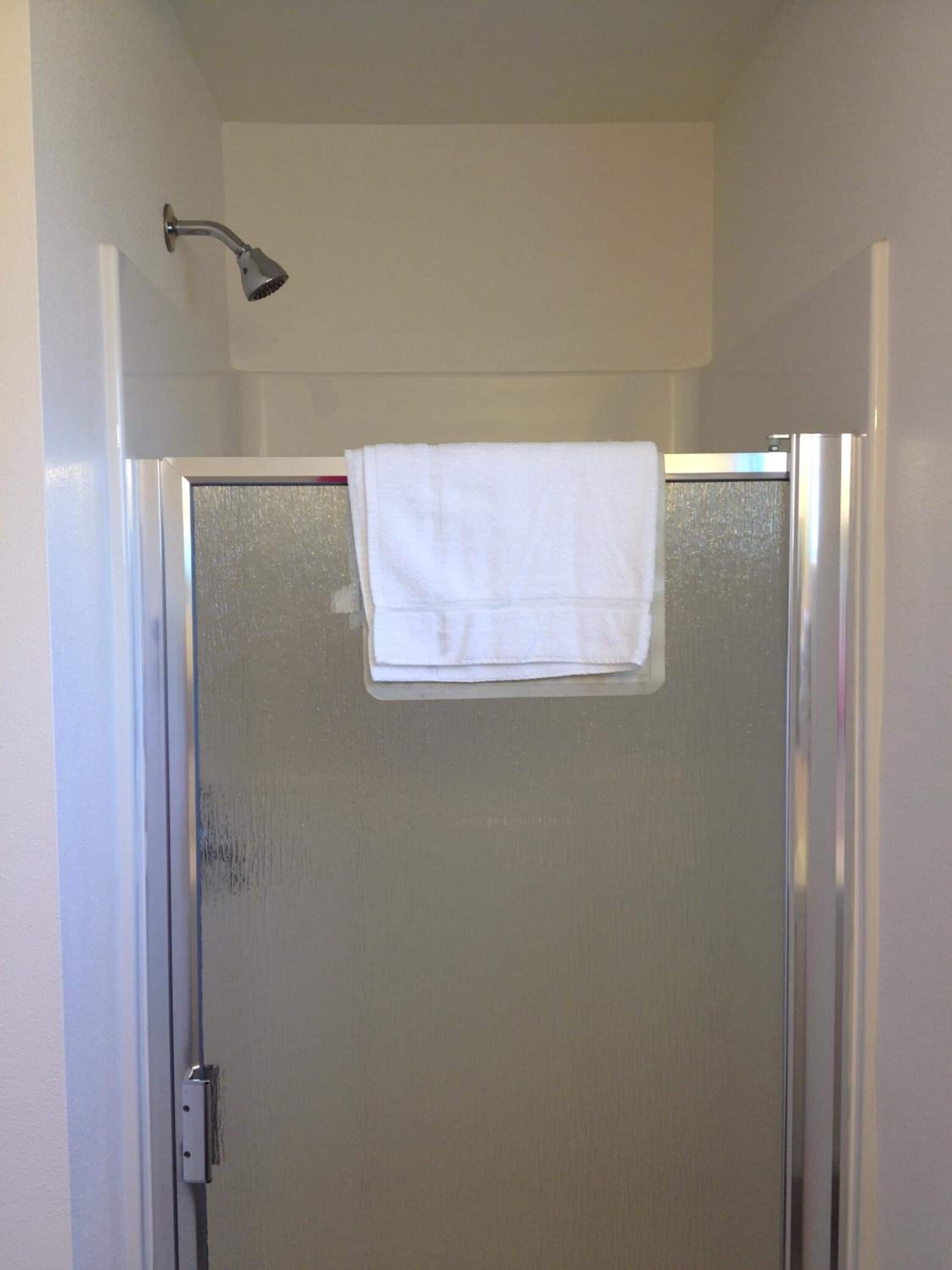 Divisória de chuveiro com porta de vidro, toalha branca pendurada na porta e chuveiro fixado na parede.