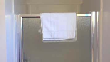 Divisória de chuveiro com porta de vidro, toalha branca pendurada na porta e chuveiro fixado na parede.