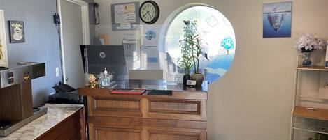 A reception desk with a clock, a bulletin board, and a window with a view of trees.