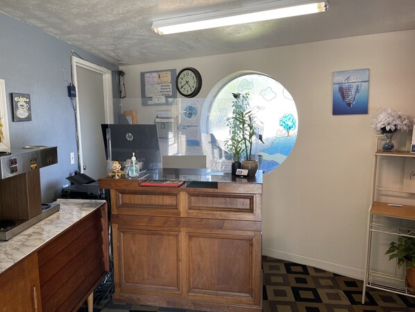 A reception desk with a clock, a bulletin board, and a window with a view of trees. - Villa West Motel (Florence)