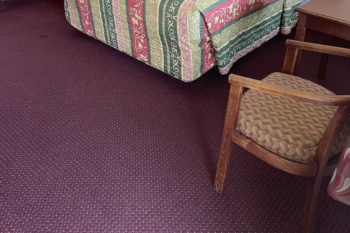 Quarto de hotel com cama, escrivaninha, cadeira e mesa de cabeceira.