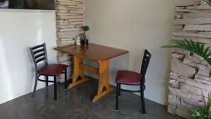 A corner room with a wooden table and two chairs, a stone wall, a cross on the wall, and a small potted plant. - Longview Inn (Longview)