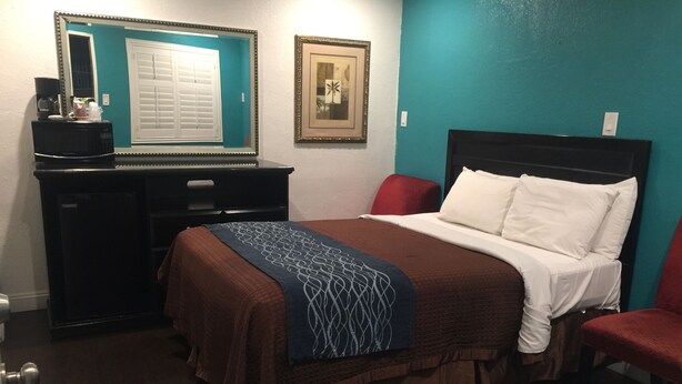 A hotel room with a bed, a desk, a chair, a mirror, and a framed picture on the wall. - Crenshaw Inn Motel (Los Angeles)