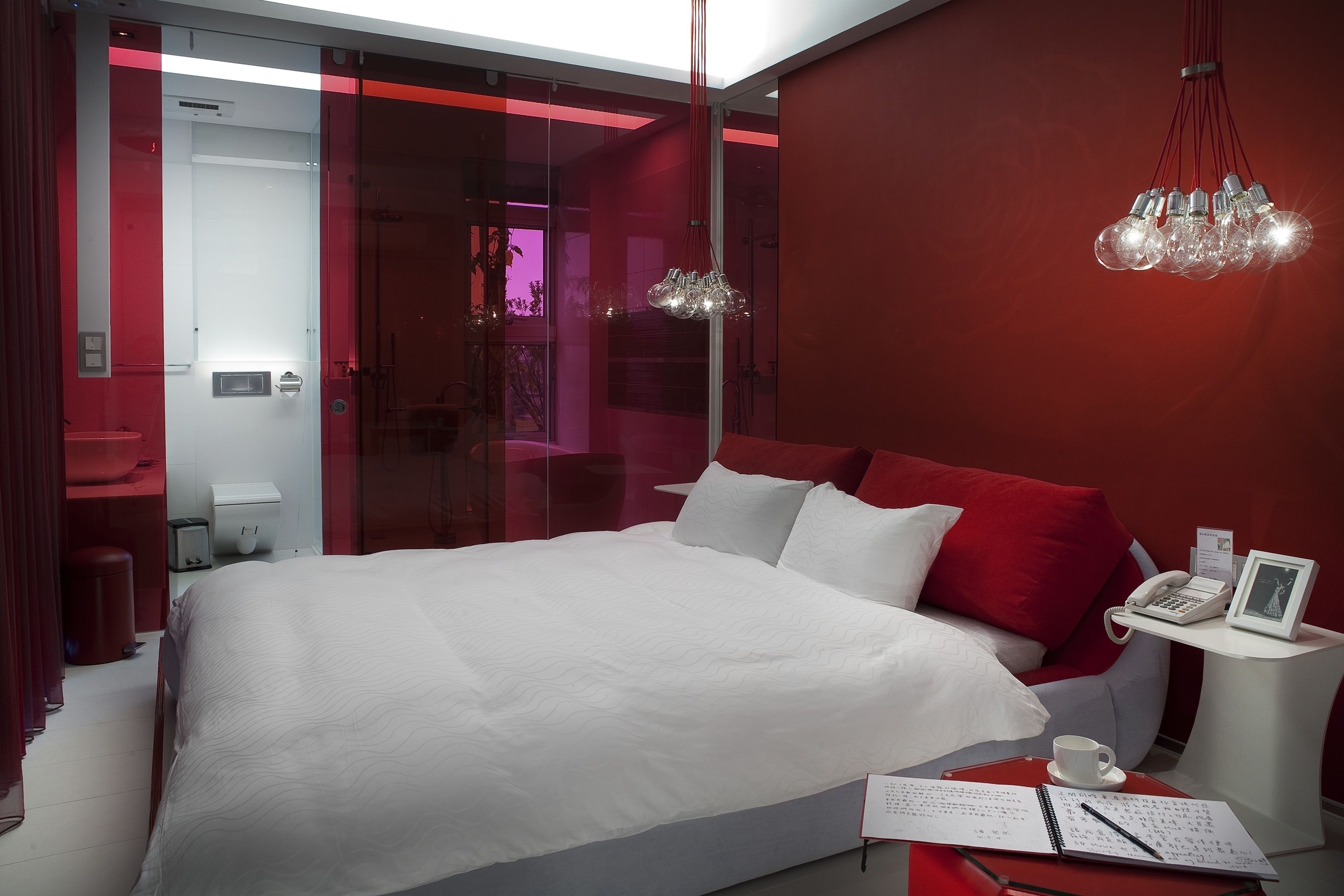 Une chambre à coucher moderne avec un grand lit, une table de chevet avec un téléphone et un cadre photo, et un mur d’accent de couleur rouge.