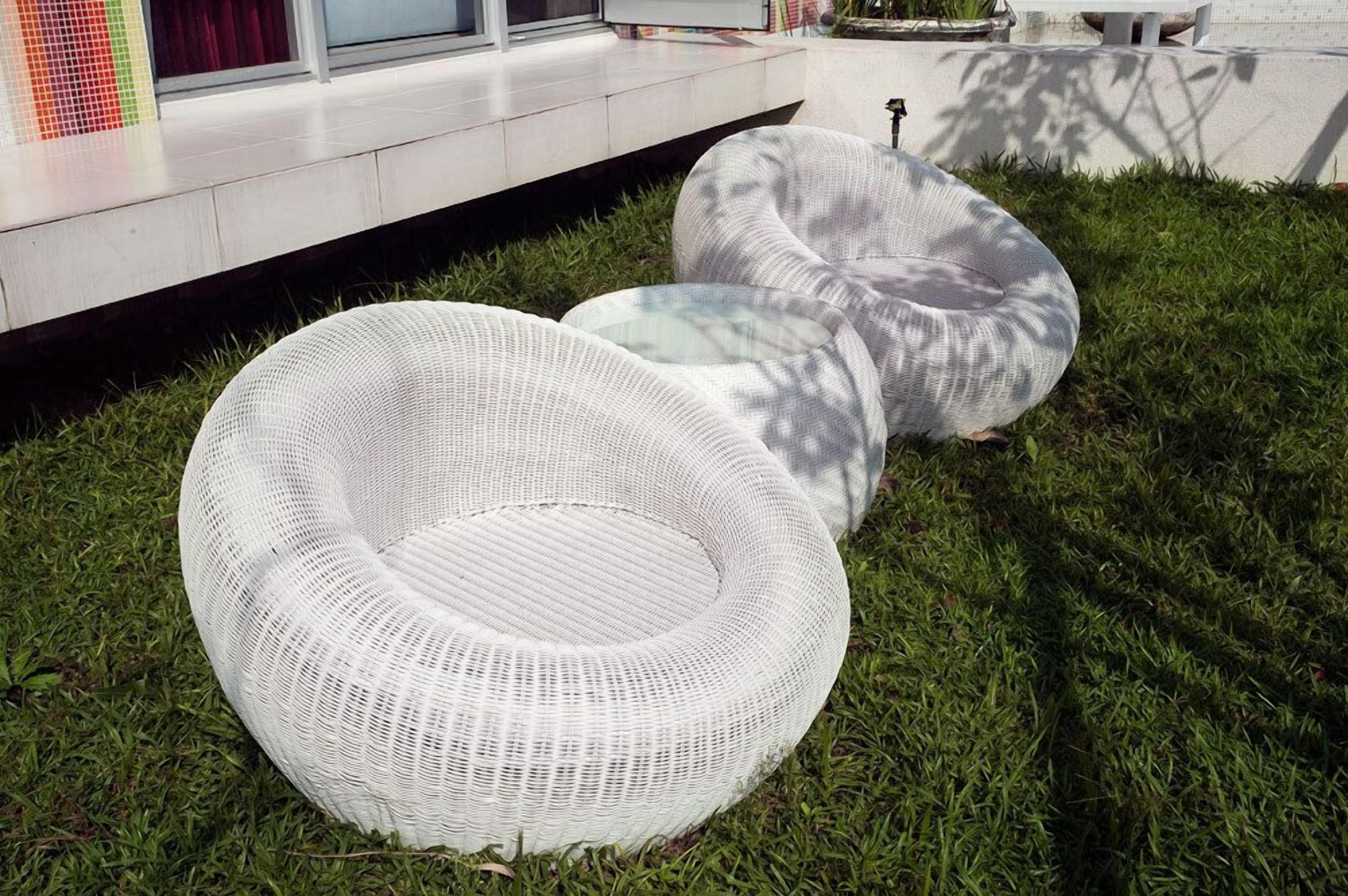 Deux chaises en osier blanc, dotées d’assises en verre, sont placées sur une pelouse verdoyante.