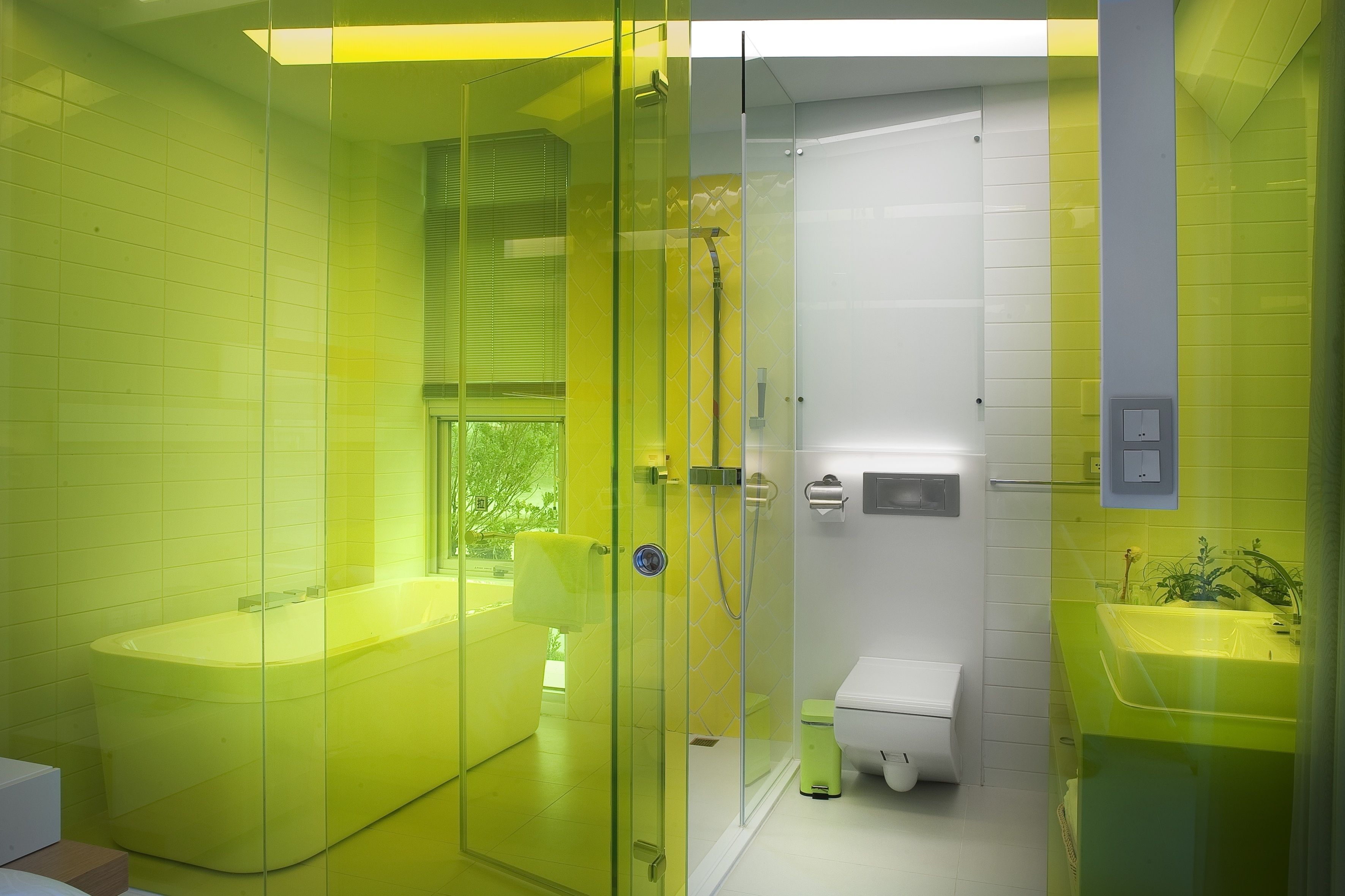 A modern bathroom with a glass-enclosed shower, a yellow bathtub, and a white toilet.
