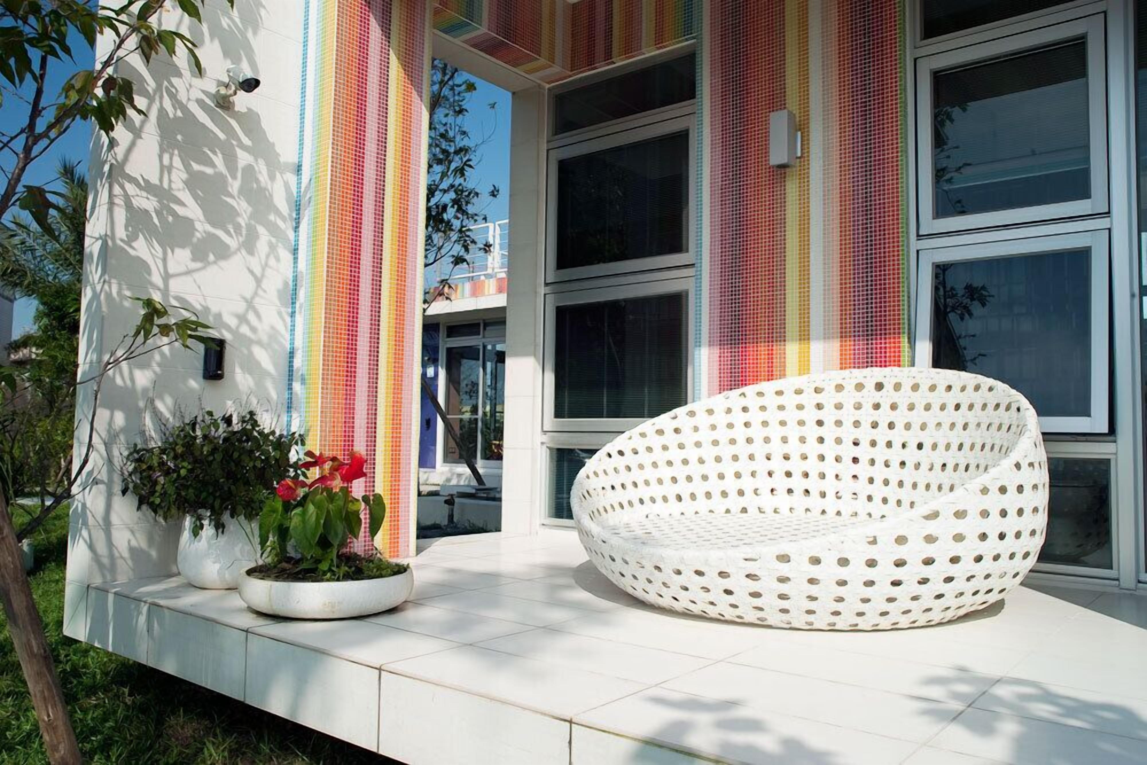A modern building with large windows and a white, perforated chair on the porch.