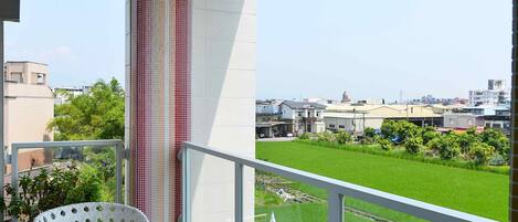A balcony with a view of a green field and buildings, white wicker furniture, and a colorful striped ceiling.
