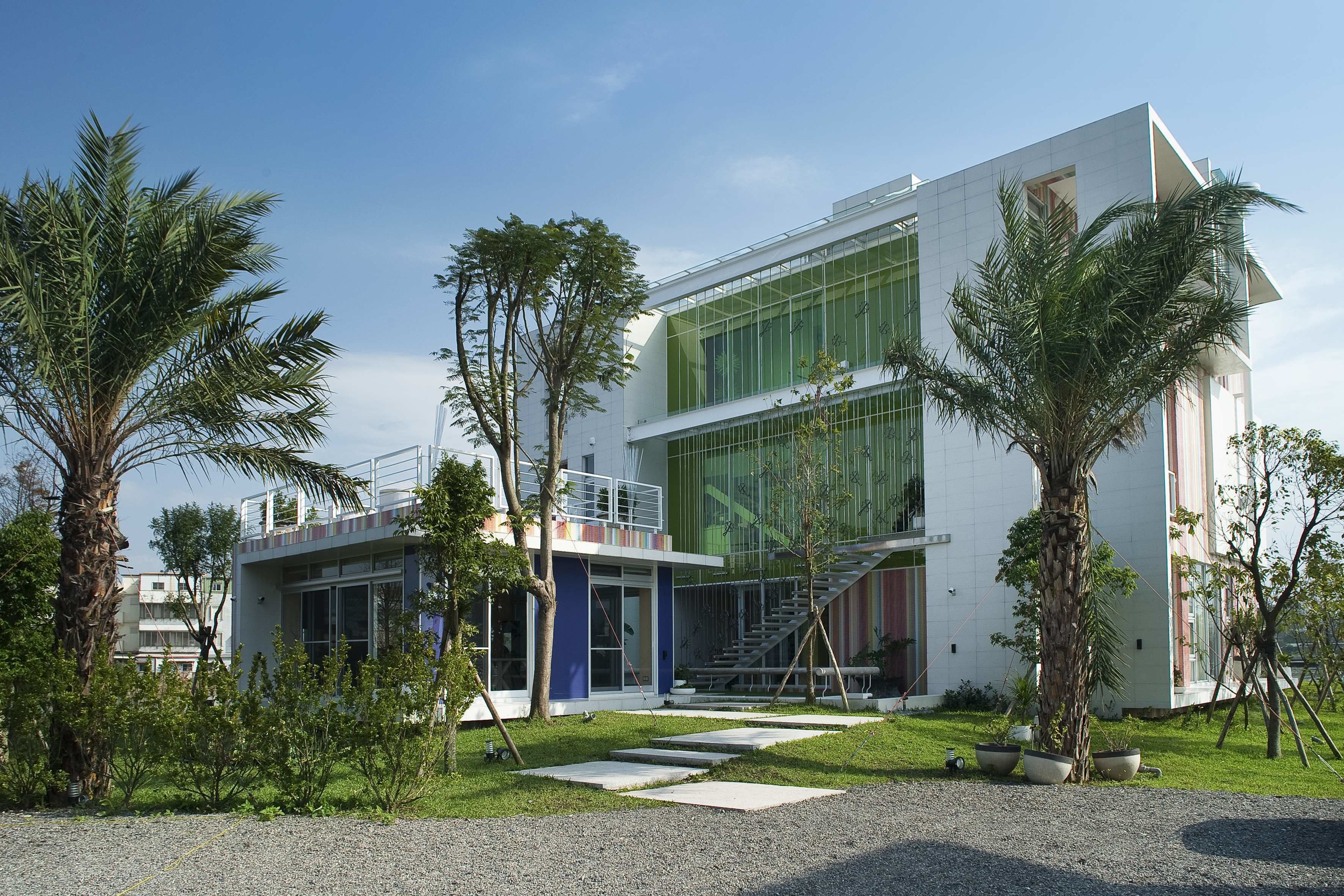 A modern building with a glass facade, a staircase, and a well-maintained garden with palm trees.