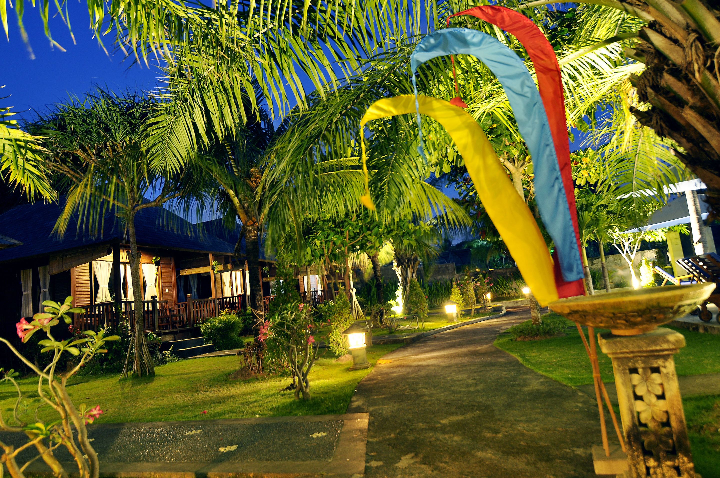 A well-lit pathway leading to a building with a wooden porch and a fountain.