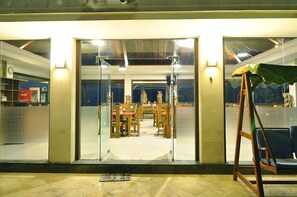 A dining area with a wooden table and chairs, a green-covered swing chair, and a tiled floor.