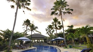 A pool area with lounge chairs, umbrellas, and palm trees. - Aman Gati Hotel Balangan (Jimbaran)