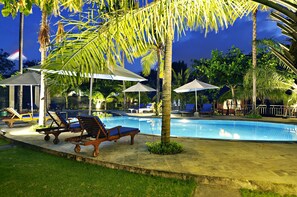 A swimming pool with lounge chairs and umbrellas, surrounded by palm trees and greenery.
