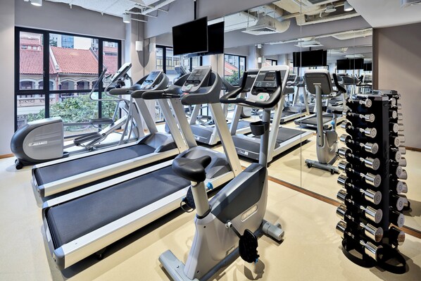 Une salle de sport équipée de tapis de course, de vélos d’exercice et d’une série de haltères.