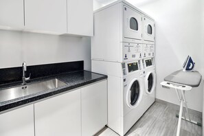 Une buanderie moderne équipée d’un lave-linge et d’un sèche-linge superposés, d’un évier et d’un petit espace dédié au repassage.