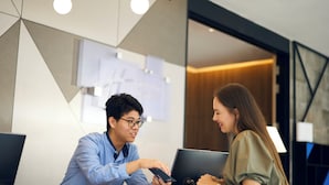 Un espace d’accueil avec un bureau, un ordinateur portable et un smartphone. Des documents sont accrochés au mur, et un luminaire moderne est installé au plafond.