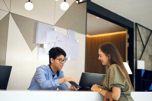 Een receptie met een bureau, een laptop en een smartphone. Er zijn papieren aan de muur en een modern lamp.