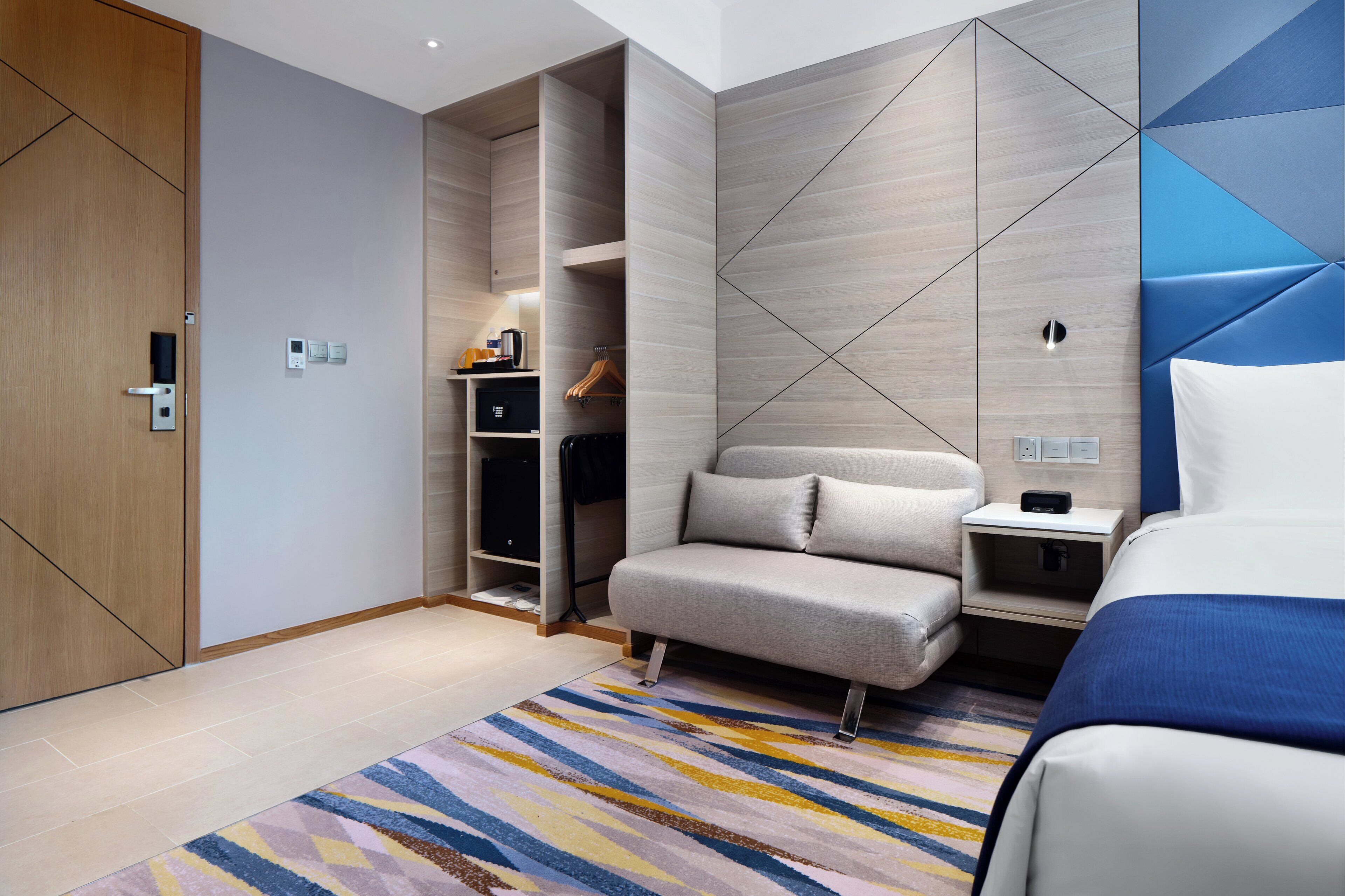 Una habitación de hotel moderna con sofá, cama, mesita de noche, armario y televisión empotrada.