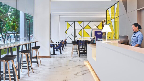 Un hall d’hôtel moderne avec un comptoir d’accueil, un espace salon et de grandes fenêtres.