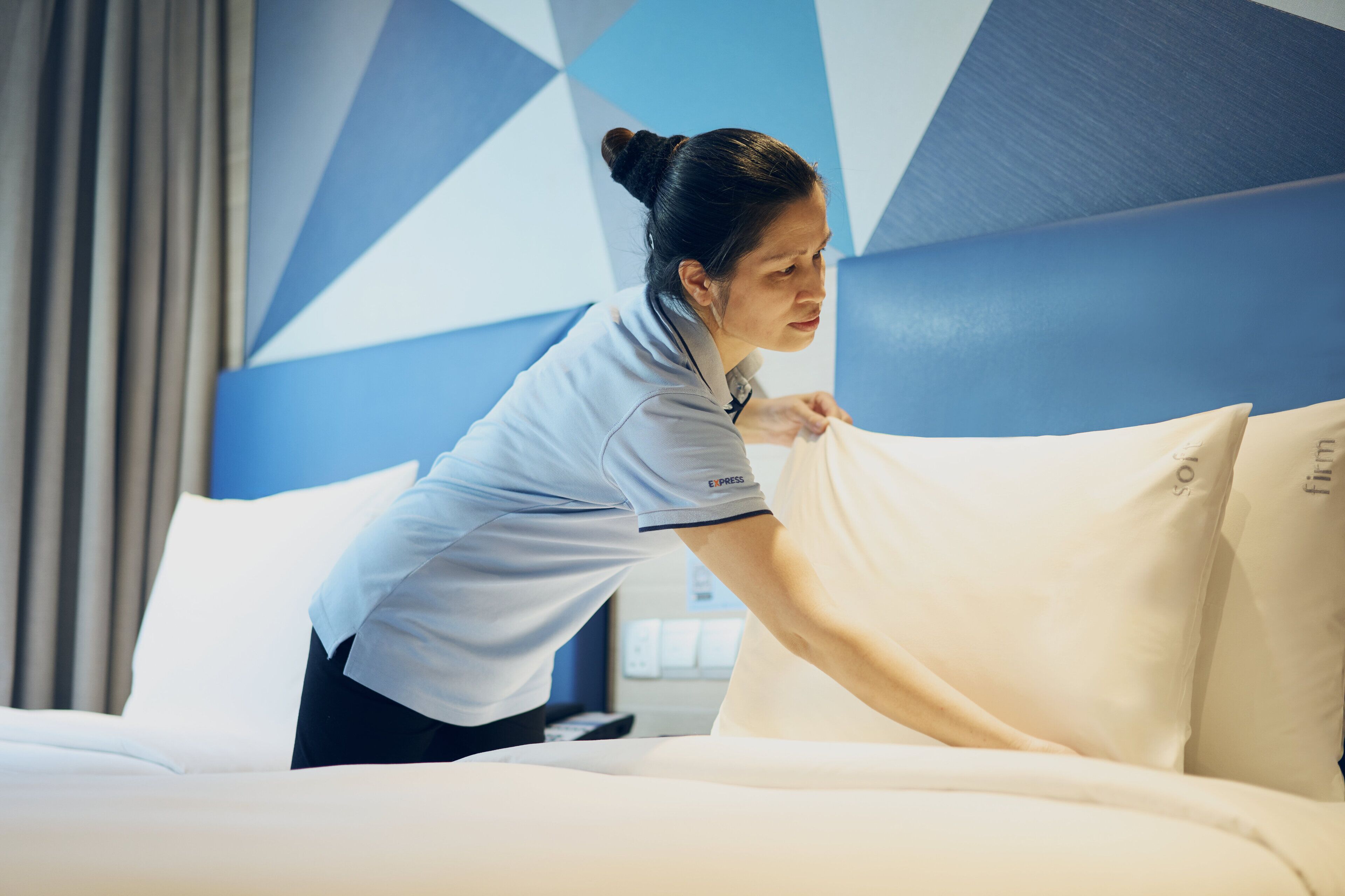 A hotel room with a bed, pillows, and a modern geometric wall design.
