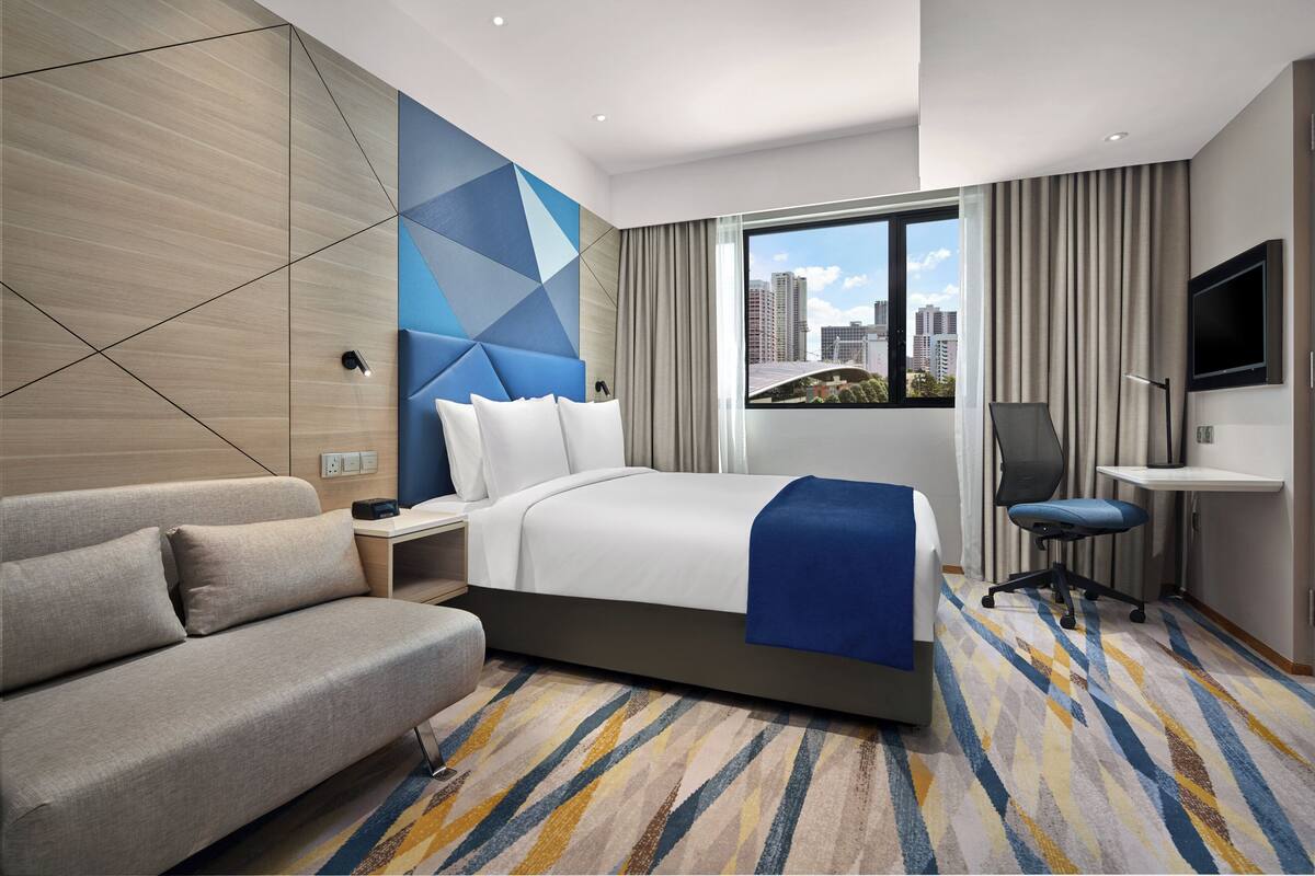 Une chambre d’hôtel comprenant un lit, un canapé, un bureau, une chaise, une télévision et donnant sur la ville.