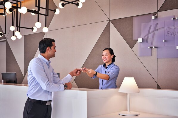 A reception desk with a modern geometric wall design, a desk lamp, and a sign indicating a holiday experience. - Holiday Inn Express Singapore Serangoon by IHG (Singapore)