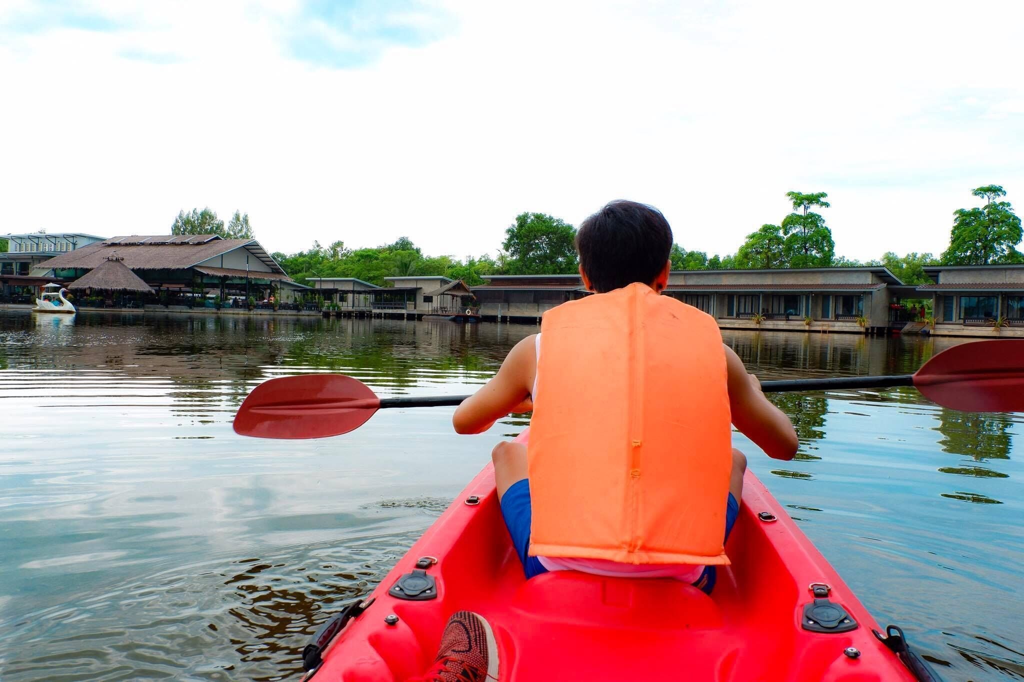 A person in a red kayak on a calm body of water, wearing an orange life jacket.