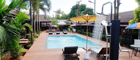 Un área de piscina con una piscina rectangular, sillas de descanso y una fuente de agua.