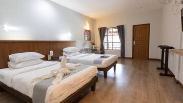 A hotel room with two beds, a bedside table, a small table with a vase, a window with curtains, and a door.