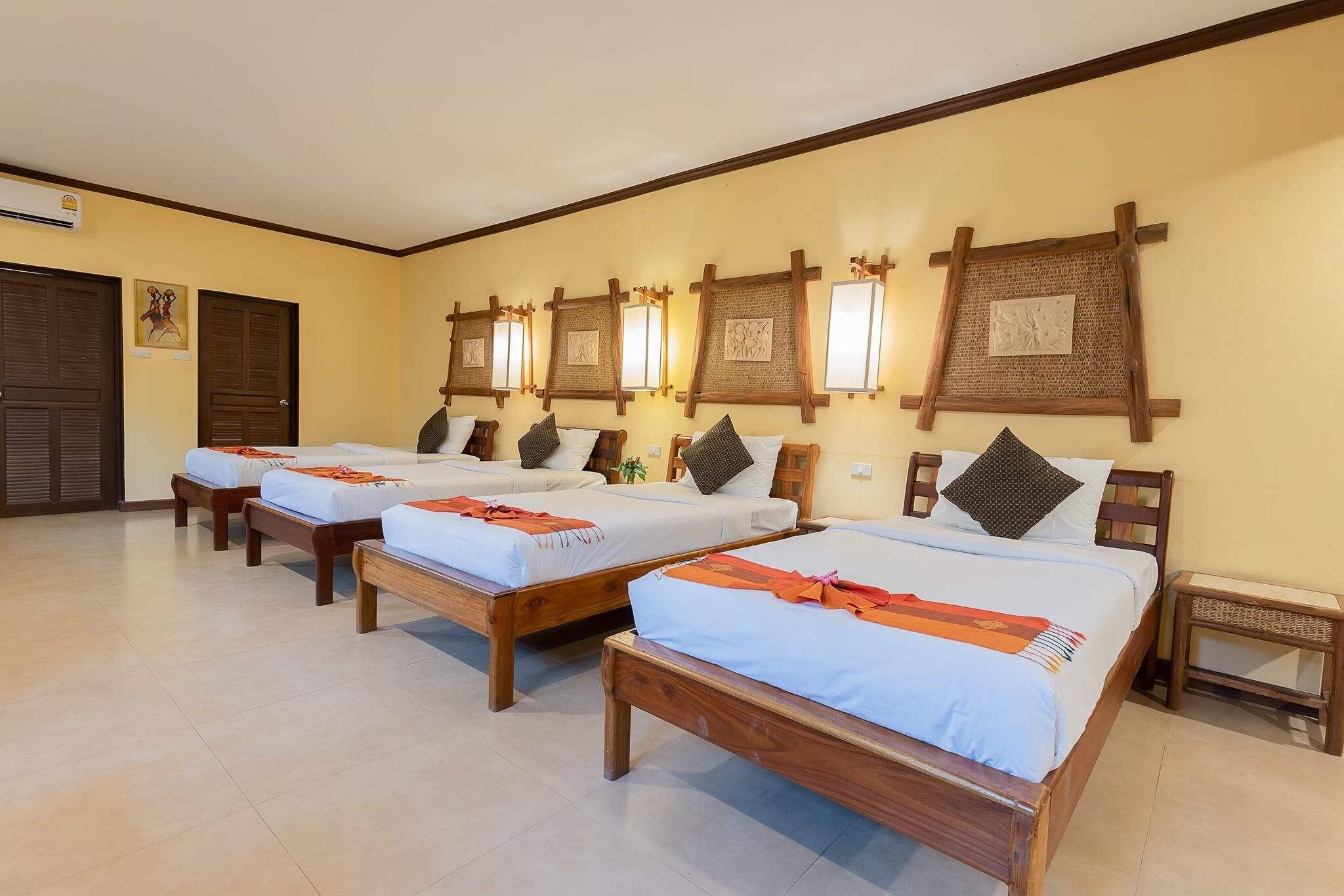 A hotel room with four single beds, wooden headboards, and wall-mounted lamps.