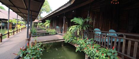 A wooden structure with a covered walkway, potted plants, and a small water body.