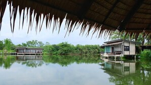 A tranquil lakeside property with a thatched roof structure, reflecting the surrounding greenery and buildings. - Banpu Resort Trat (Trat)