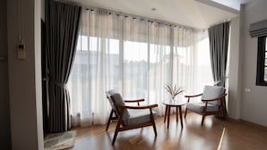 A modern living room with wooden flooring, a sofa, two armchairs, a small table, and a potted plant. - Banpu Resort Trat (Trat)