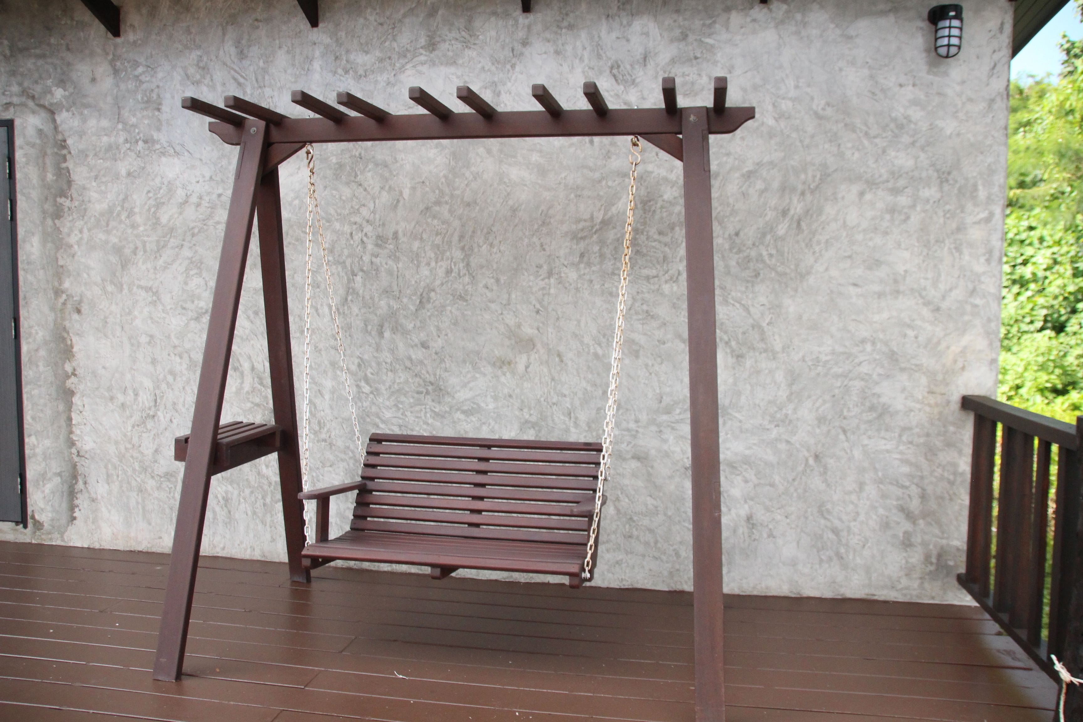 A wooden swing set with a bench on a wooden deck against a textured wall.