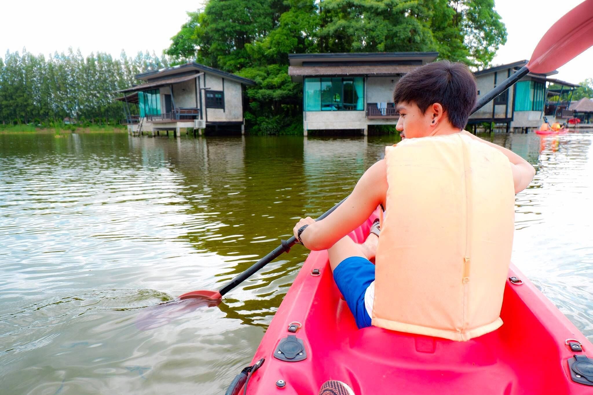 A person in a red kayak on a calm body of water with houses on stilts in the background.
