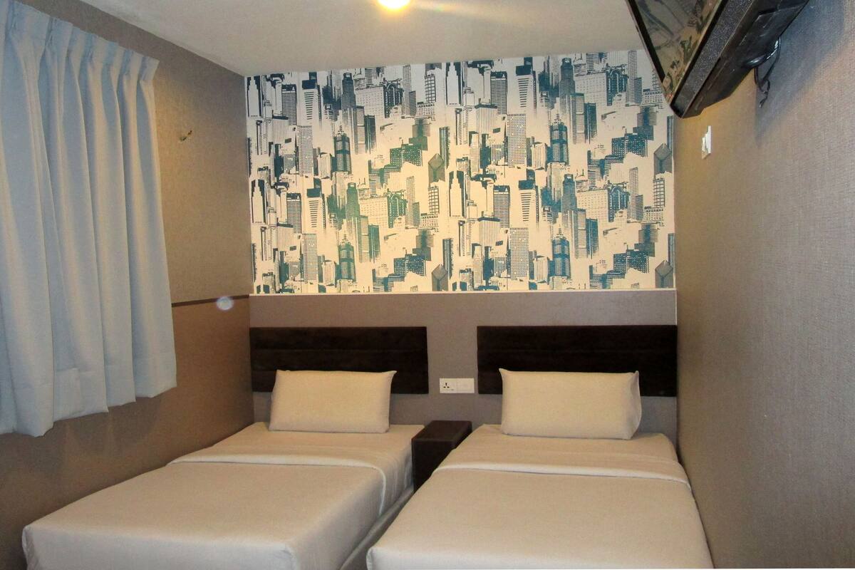 A hotel room with two beds, a cityscape wallpaper, and a curtain.