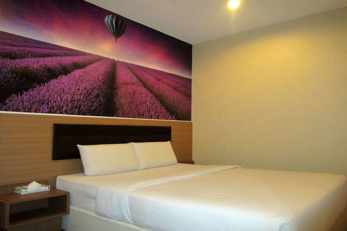 A hotel room with a large bed, a nightstand, and a wall mural of a lavender field with a hot air balloon.