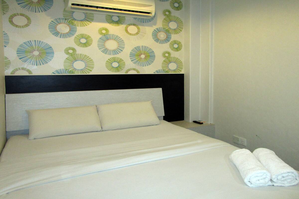 A hotel room with a bed, pillows, a headboard, an air conditioning unit, and a wall with circular patterns.